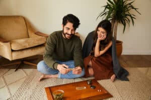 Smiling young man rolling a joint while getting high with his girlfriend on their living room floor at home