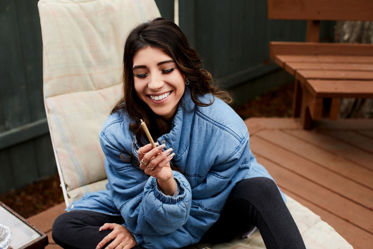 Young woman laughing while sitting alone outside on her patio and smoking a joint