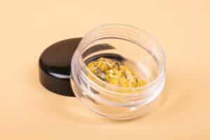 golden cannabis dab in glass container, wax extract on yellow background.