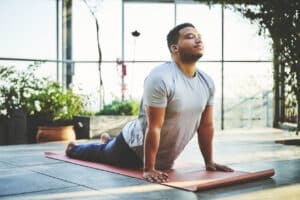 Mid adult man practicing Upward Facing Dog Pose. Handsome fit male is doing yoga on exercise mat. He is in sportswear.